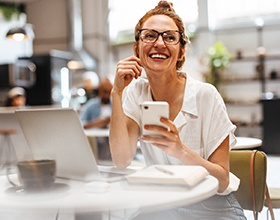 Woman smiling while working on laptop and phone
