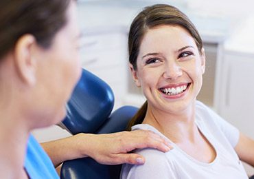 Young woman in dental chair smiling at dental team member