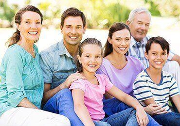 Three generations of family smiling outdoors after dental office visit