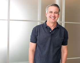 Man with greying hair and in navy polo smiling