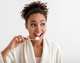 Woman smiling while brushing her teeth in white robe