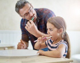 Young girl and her father brushing their teeth together