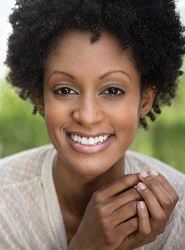 Young woman in light brown shirt grinning outdoors