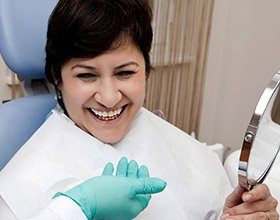 Woman examining her smile after restorative dentistry with dental implants