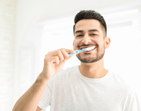 Man smiling while brushing his teeth in bathroom