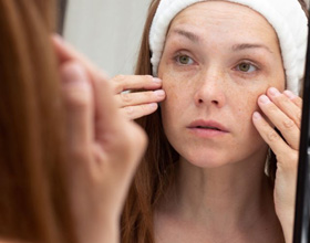 Woman looking at herself in mirror, concerned about wrinkles