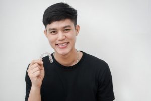 young man smiling while holding Invisalign in Chesterfield 