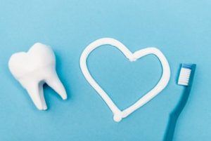 A tooth, a heart drawn with toothpaste and a blue toothbrush laying against a light blue background